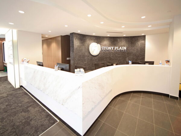 A modern reception area featuring a curved white marble desk with a logo on the wall behind it. The space is well-lit, with gray flooring and minimalist decor, creating a welcoming atmosphere.
