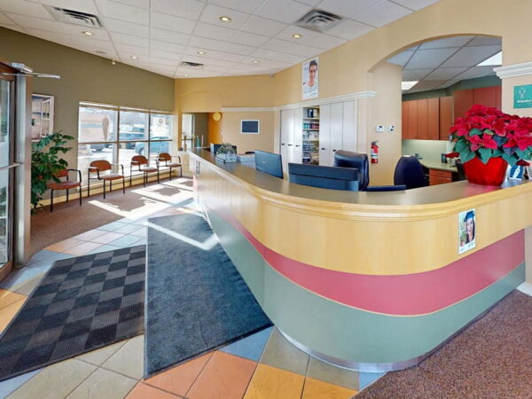 A bright and welcoming reception area featuring a curved front desk, colorful floor tiles, and comfortable seating. The space is well-lit with large windows and decorative plants, creating an inviting atmosphere for visitors.