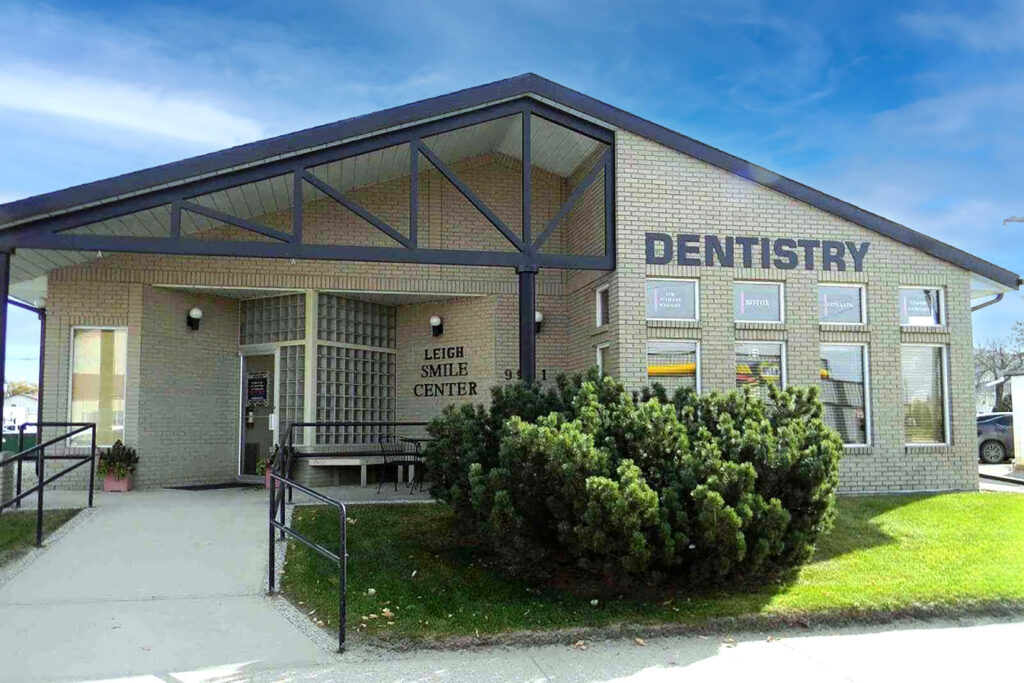 A modern dental office building with large windows, a welcoming entrance, and the word "DENTISTRY" prominently displayed on the facade. The surroundings feature well-maintained greenery, creating an inviting atmosphere for patients.