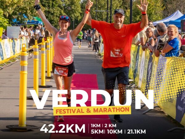 A man and woman celebrate as they cross the finish line together at the Verdun Festival & Marathon. Both are smiling and raising their arms in triumph amidst a crowd of spectators, with banners displaying the event details in the background.