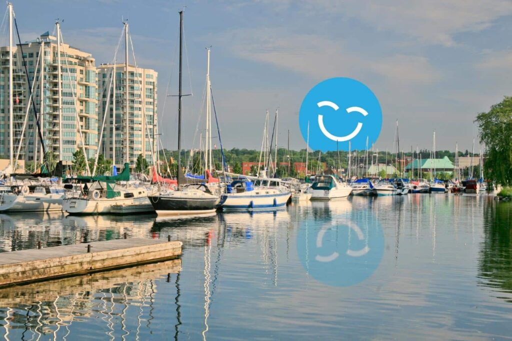 A serene marina scene featuring multiple sailboats docked in calm waters, with modern buildings in the background and a cheerful smiley face overlaid in blue.
