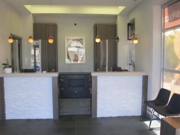 A modern reception area featuring a light-colored stone counter, dark cabinets, and stylish pendant lighting. There are two black chairs for seating and a large window showcasing an image of a woman outside.