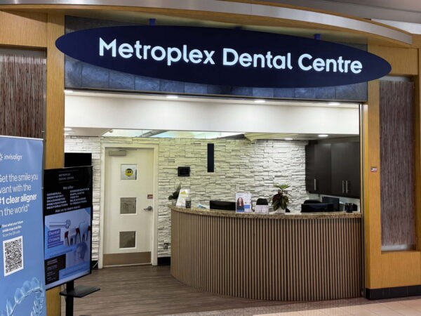 Entrance of Metroplex Dental Centre, featuring a welcoming reception area with a curved desk, modern decor, and informational displays. The sign clearly indicates the name of the dental center.