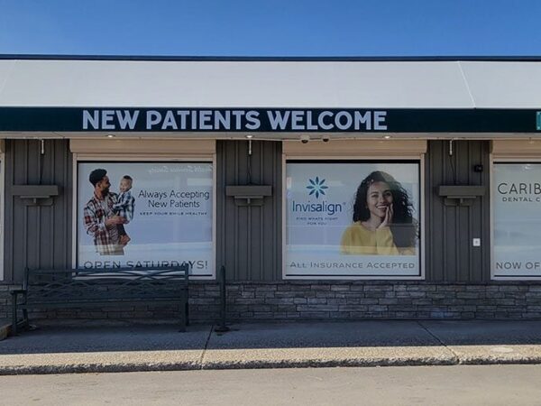 Dental clinic storefront with large window advertisements featuring diverse models. Signs indicate "new patients welcome."