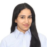 A woman with long black hair is smiling. She is wearing a light blue button-up shirt. The background is plain white, highlighting her friendly expression.