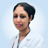 A professional woman wearing a white lab coat smiles gently against a soft blue background. She appears approachable and confident, suggesting expertise in her field.
