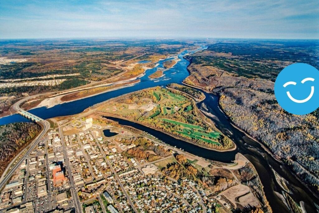 Aerial view of a landscape featuring winding rivers, lush greenery, and a small town adjacent to the water. The scene highlights the natural beauty of the area, with rolling hills and a clear blue sky in the background.