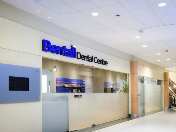 Une zone d'accueil moderne de clinique dentaire présentant l'enseigne « Bental Dental Centre. » L'espace est bien éclairé, avec des murs en verre et une atmosphère accueillante.