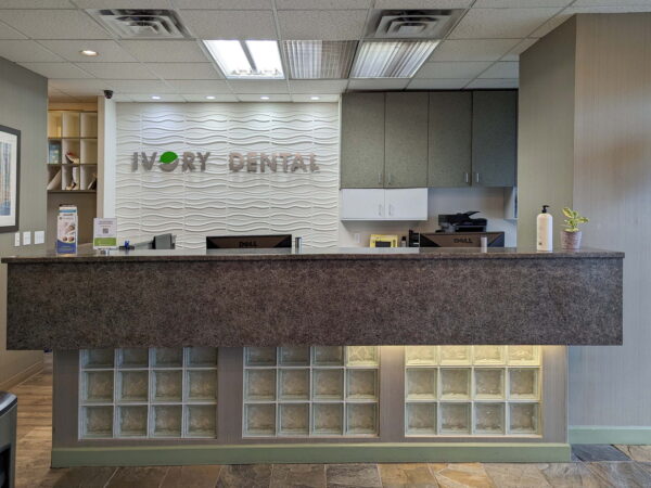 A modern dental office reception area featuring a sleek, dark countertop and a textured wall with the words "Ivory Dental." The space is well-lit and has a clean, professional appearance.