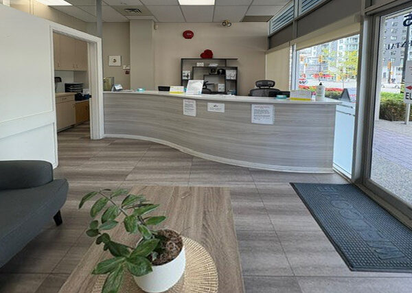 A modern dental office reception area featuring a curved counter, a waiting area with a comfortable couch, and a potted plant. Natural light filters in through large windows, creating an inviting atmosphere for patients. The 123Dentist Smiley adds a cheerful touch to the environment.