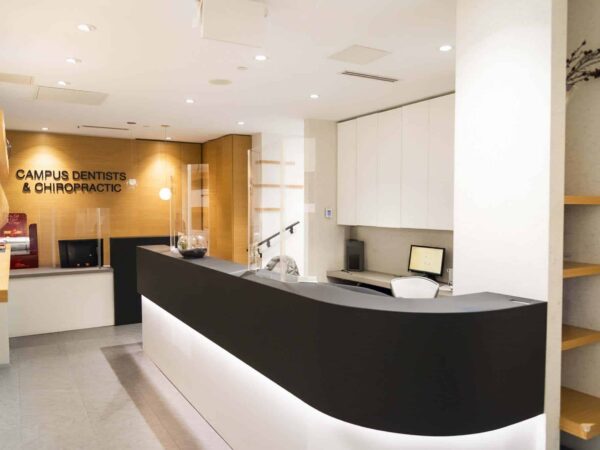 A modern dental and chiropractic reception area featuring a sleek black front desk, wooden accents, and soft lighting. The space is uncluttered, creating a welcoming environment for patients.