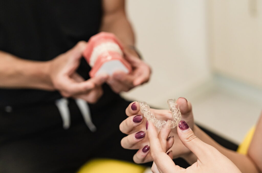 A dental professional demonstrates an orthodontic appliance while a patient holds a similar device, showcasing a dental consultation. The scene conveys a focus on oral care, emphasizing personalized treatment.