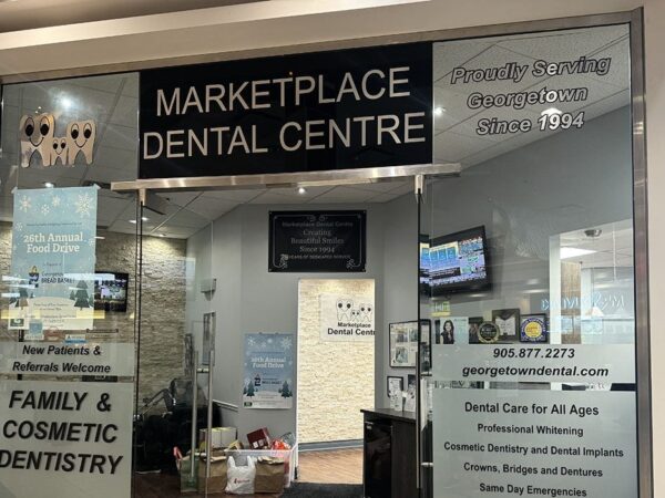 Entrance to Marketplace Dental Centre featuring glass doors with signage. The display includes information about family and cosmetic dentistry services and contact details.