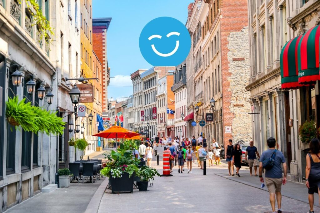 A busy, vibrant street scene with historic buildings, colorful awnings, and pedestrians enjoying a sunny day. A smiling face emoji is superimposed above the street.