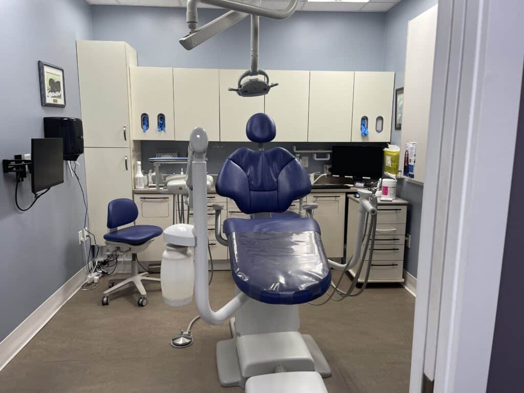 A bright dental office features a blue dental chair, equipment, and cabinets. The space is designed for comfort and efficiency, ready for patient care. A friendly 123Dentist Smiley adds a cheerful touch to the environment.