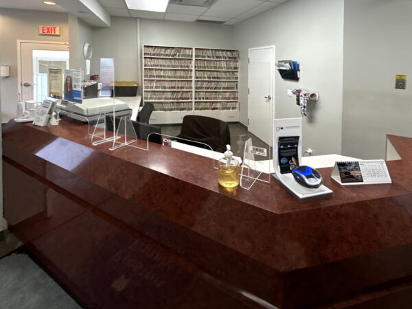An inviting dental reception area features a polished counter, health safety measures, and informational displays. A cozy atmosphere is created with a neat organization, ensuring a welcoming experience for patients visiting the 123Dentist Smiley.