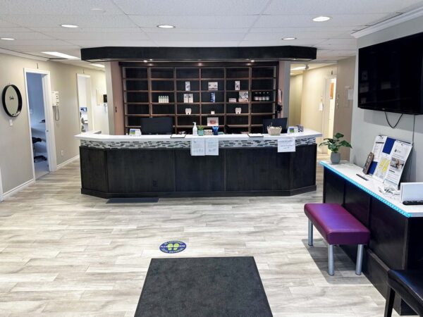A modern reception area with a granite-topped front desk, a seating area featuring a purple bench, and informational displays. The space is well-lit with light-colored walls and wooden flooring, creating a welcoming atmosphere.