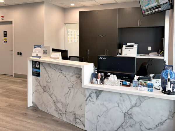 A modern dental reception area featuring a sleek marble countertop, a computer station, and welcoming decor. The space is well-lit and organized, creating a friendly atmosphere for patients, with the 123Dentist Smiley adding a cheerful touch.