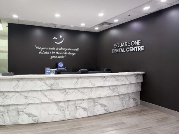 Modern dental reception area featuring a marble front desk, accented by a motivational quote on the wall. The space is well-lit with a sleek design, branded with "Square One Dental Centre."