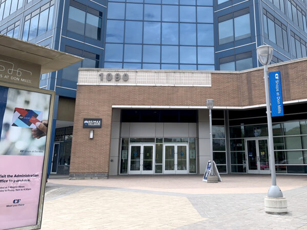 A modern building features large glass windows and an entrance marked with the number 1930. Nearby, a promotional sign displays dental services. The friendly 123Dentist Smiley adds a welcoming touch to the scene.