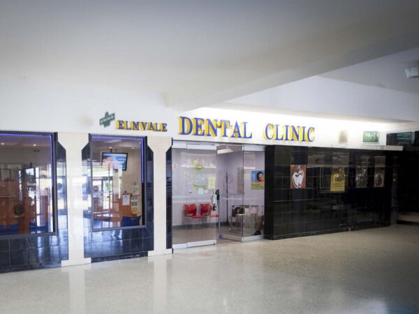 A dental clinic is visible in a brightly lit area, featuring a sign that reads "DENTAL CLINIC." The entrance is framed with glass, and the clinic is situated alongside other storefronts in a spacious interior.