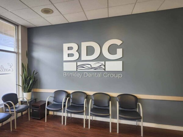 A waiting area for Brindley Dental Group featuring a grey wall with the BDG logo. The space includes several black chairs and a potted plant, creating a calm, inviting atmosphere for patients.