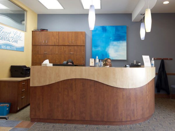 A dental reception area featuring a curved wooden front desk, modern decor, and a calming blue wall art piece. The setting is bright and welcoming, suitable for patients visiting 123Dentist.