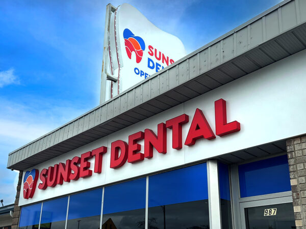 A dental office building with a prominent sign reading "SUNSET DENTAL." The exterior features large windows and a bright blue sky in the background, giving a welcoming appearance.