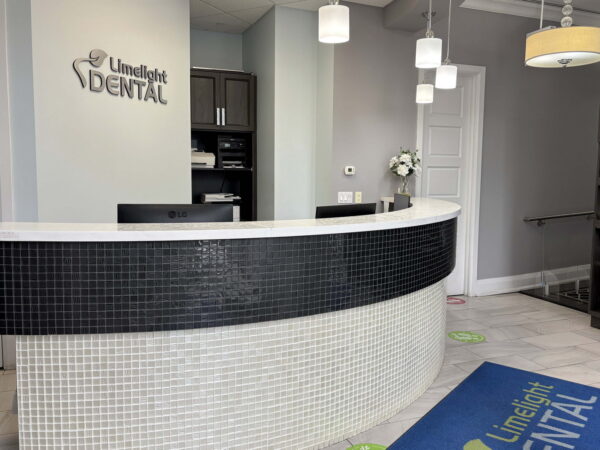 A modern dental reception area featuring a curved white and black front desk, with pendant lighting and a welcoming atmosphere. The logo "Luminous Dental" is displayed prominently on the wall, and there’s a colorful entrance mat on the floor.