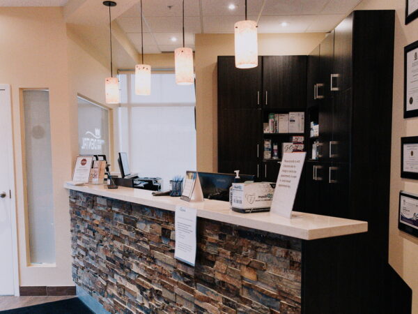 A modern dental office reception area featuring a stone countertop, illuminated pendant lights, and a variety of dental products and informational signage displayed. The inviting atmosphere promotes a welcoming environment for patients.