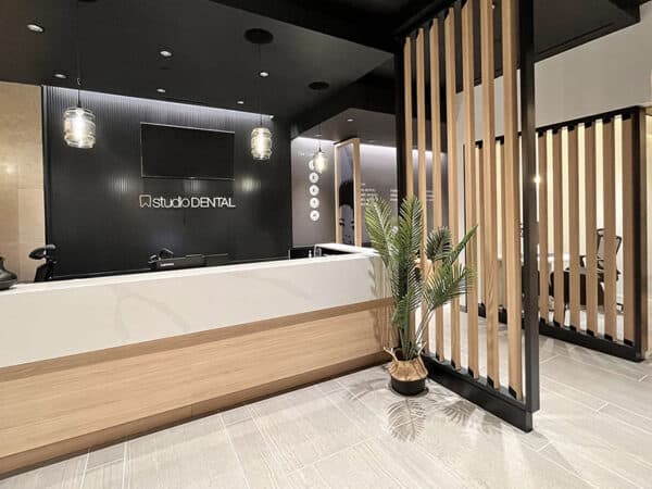 A modern dental office reception featuring a sleek white front desk, warm wood accents, and stylish black walls. Soft lighting creates a welcoming ambiance, complemented by a decorative plant. The 123Dentist Smiley adds a friendly touch to the inviting space.