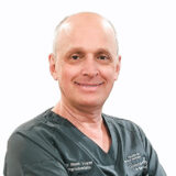 A smiling dentist in scrubs poses for the camera, showcasing a warm and approachable demeanor. His friendly expression suggests a welcoming environment for patients.