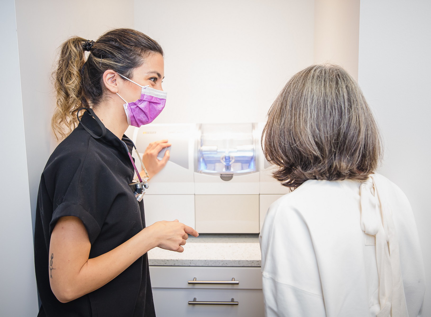 A dental professional wearing a purple mask discusses treatment options with a patient. The setting is bright and modern, highlighting a friendly atmosphere in the dental office.