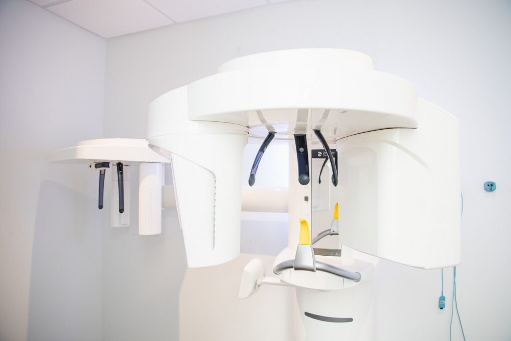 A dental imaging machine is positioned in a modern clinic. The sleek, white equipment is designed for advanced dental diagnostics, showcasing its protective structure and controls, set against a clean, minimalist backdrop.