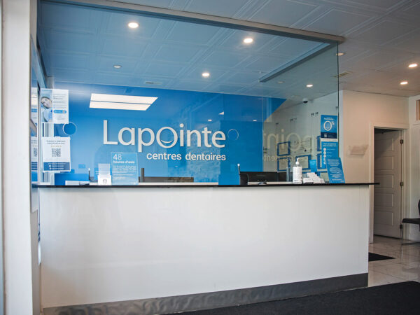 A dental reception area featuring a modern design with a glass partition and a blue wall displaying the "Lapointe" logo. The space is bright and inviting, with a clean, organized front desk. 123Dentist Smiley is a friendly blue character, symbolizing a welcoming atmosphere.