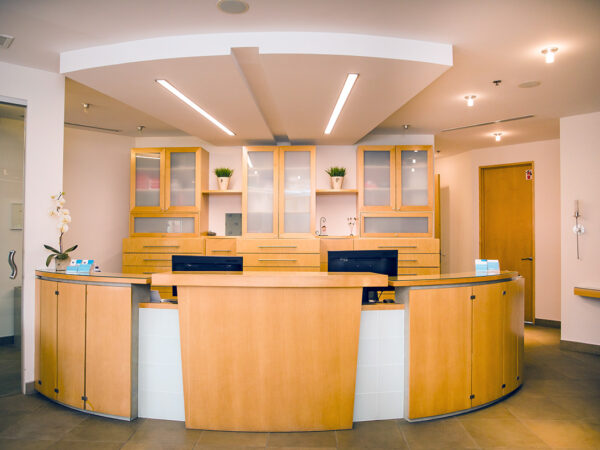 A modern dental office reception area featuring a warm wooden front desk, neatly organized shelves, and bright lighting. The space offers a welcoming atmosphere, suitable for patients. A friendly 123Dentist Smiley adds a cheerful touch to the environment.