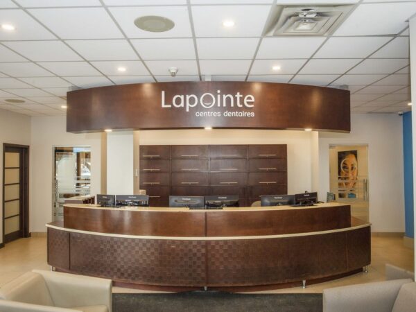 The image shows a modern reception area with a curved wooden desk labeled "Lapointe." The space is well-lit and features a minimalist design, including comfortable seating and a neutral color palette, creating a welcoming atmosphere for visitors.
