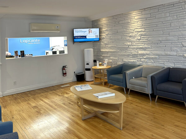 A cozy dental office waiting area featuring blue armchairs, a wooden coffee table, and a reception desk with an informational screen. The walls are subtly textured, and the space is bright and inviting for patients. The friendly 123Dentist Smiley adds a cheerful touch to the environment.
