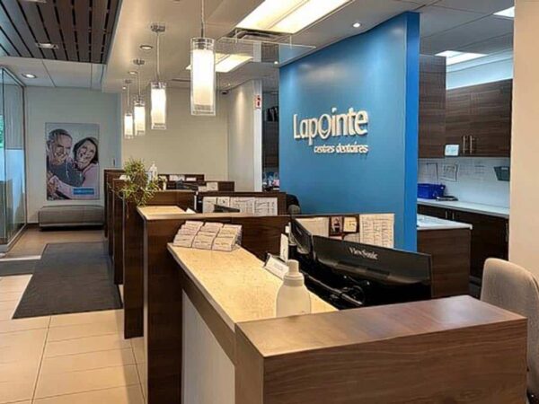 The image shows a modern office reception area with wooden counters and a blue wall featuring the logo "Lapointe." The space is well-lit, featuring pendant lights and seating visible in the background.