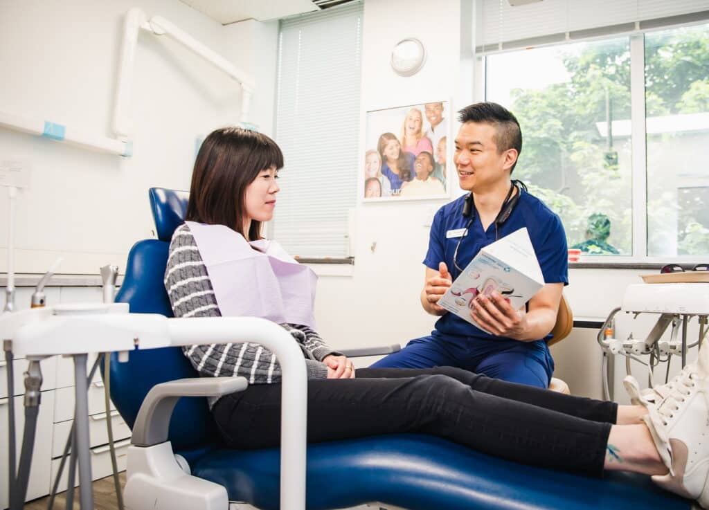 A dental professional is seated with a patient in a modern clinic, discussing treatment options. The patient appears attentive and engaged, while the doctor holds a brochure. Natural light fills the room, creating a welcoming atmosphere. A friendly 123Dentist Smiley is present to convey a positive experience.