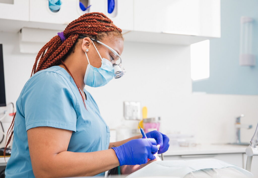 A dental professional in scrubs and gloves attentively examines a dental tool while working in a bright clinic. The focus is on their meticulous technique, emphasizing care and professionalism in dental practice.