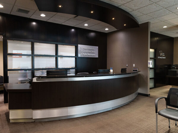 A modern dental office reception area with a curved front desk, soft lighting, and comfortable seating. The space is well-organized, featuring a clean design and a welcoming atmosphere.
