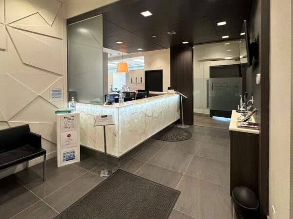 A modern reception area featuring a sleek front desk with a light-colored surface, a waiting bench, and a display board. The walls are adorned with contemporary design elements, and the space is well-lit, creating an inviting atmosphere.