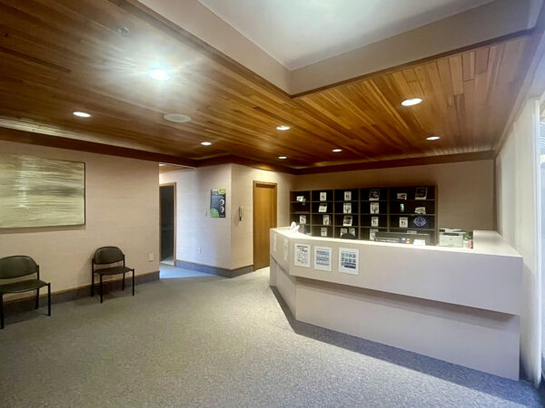 A welcoming reception area featuring a wooden ceiling, two chairs on the left, a front desk with informational materials, and soft lighting, creating a warm and inviting atmosphere.