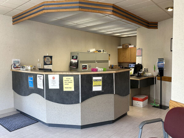 A dental reception area with a curved front desk, informational signage, and a waiting area featuring a chair. The space is well-lit and organized, creating a welcoming environment for patients.