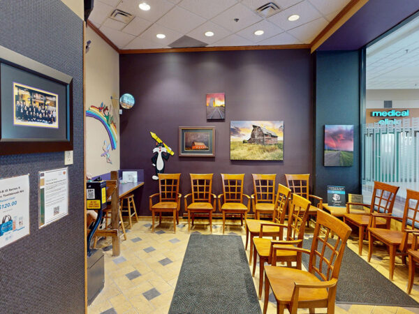 A dental waiting room featuring wooden chairs arranged in rows, colorful artwork on the walls, and a cozy atmosphere. Natural light filters in through large windows, creating a welcoming environment for patients.