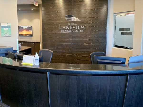 A modern reception area featuring a dark wooden front desk with a sign that reads "Lakeview Dental Center." Soft lighting and neutral colors create a welcoming atmosphere. A bottle of hand sanitizer is visible on the desk.