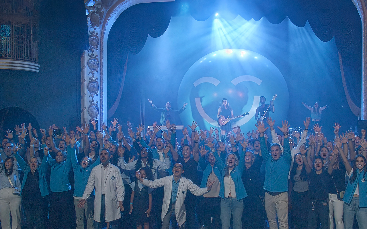Une foule animée célèbre joyeusement le lancement de la campagne « Smiles Across Canada » (Des sourires à travers le Canada), levant les mains avec enthousiasme. À l'arrière-plan, un artiste joue de la guitare sur scène, accompagné d'un éclairage coloré et d'un grand smiley 123Dentiste qui ajoute une touche ludique à l'atmosphère.