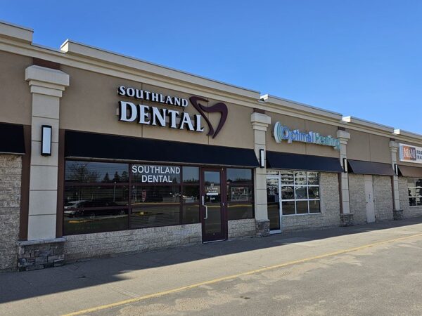Exterior view of a dental clinic named "Southland Dental," featuring a modern storefront with clear signage. Nearby storefronts can also be seen under a clear blue sky.