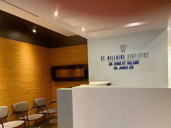 An interior view of a dental clinic reception area, featuring modern decor with wooden accents, a seating area with chairs, and a reception desk displaying the clinic's name and dentist details.